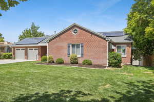 Ranch-style house with roof mounted solar panels, concrete driveway, an attached garage, and a front yard