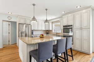 Kitchen with stainless steel appliances, a center island, light stone countertops, backsplash, and light wood-style floors