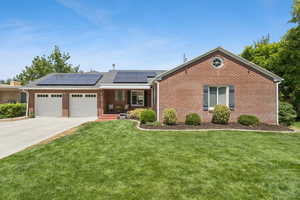 Ranch-style house featuring solar panels, a front lawn, brick siding, a garage, and driveway