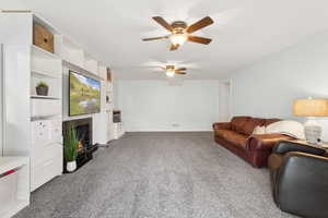 Carpeted living area featuring a ceiling fan and a fireplace with flush hearth