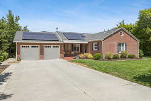 Single story home with an attached garage, a front lawn, driveway, brick siding, and solar panels