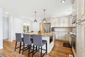 Kitchen with a breakfast bar, light stone counters, a center island with sink, stainless steel appliances, and light wood-style floors