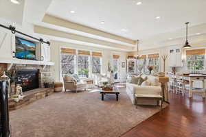 Living room featuring a tray ceiling, dark wood finished floors, recessed lighting, a fireplace, and a barn door