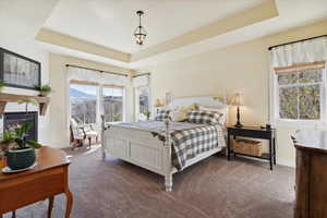 Bedroom with a raised ceiling, dark carpet, a glass covered fireplace, and a mountain view
