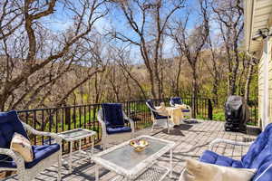 View of patio with an outdoor living space, grilling area, a wooden deck, and a view of trees