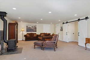 Living area with a wood stove, light carpet, recessed lighting, and a barn door