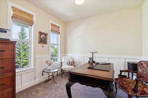 Living area featuring a decorative wall, wainscoting, a desk, and carpet floors