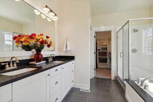 Full bath featuring healthy amount of natural light, double vanity, a shower stall, and a spacious closet