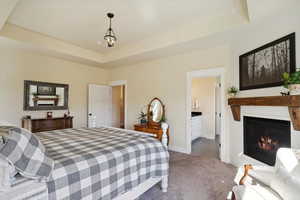 Carpeted bedroom with a glass covered fireplace, a tray ceiling, and a chandelier
