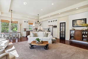 Living area with a tray ceiling, a chandelier, dark wood-type flooring, and recessed lighting