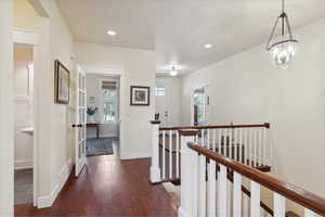 Hallway featuring an upstairs landing, dark wood-style flooring, and recessed lighting