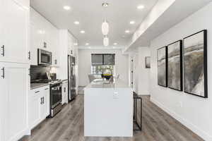 Kitchen featuring appliances with stainless steel finishes, a center island with sink, white cabinetry, light wood-style floors, and recessed lighting