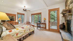 Carpeted bedroom featuring a stone fireplace, access to exterior, and a ceiling fan