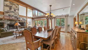 Dining area featuring light wood finished floors, a textured ceiling, a chandelier, a stone fireplace, and recessed lighting