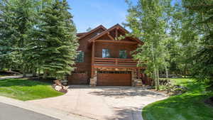 View of front of house featuring stone siding, driveway, an attached garage, and a front lawn