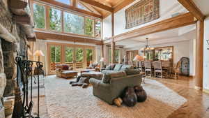 Living area with a wooden ceiling with exposed beams, plenty of natural light, wood-type flooring, a chandelier, and a stone fireplace