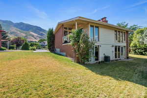 Back of house with a lawn, a chimney, brick siding, and a mountain view