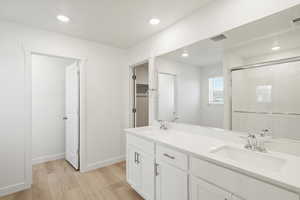 Full bathroom featuring light wood-type flooring, a shower stall, double vanity, recessed lighting, and a spacious closet
