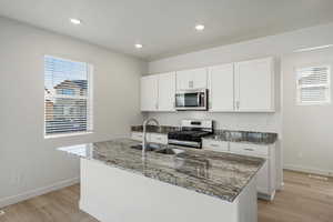 Kitchen with dark stone countertops, stainless steel appliances, white cabinets, light wood finished floors, and recessed lighting