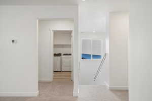Corridor featuring an upstairs landing, light colored carpet, and separate washer and dryer