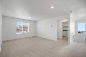 Unfurnished room with light carpet, a textured ceiling, independent washer and dryer, and recessed lighting