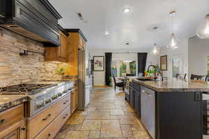 Kitchen featuring a kitchen bar, decorative light fixtures, dark stone countertops, stainless steel appliances, and a kitchen island with sink
