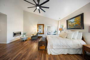 Bedroom with hardwood / wood-style floors, a glass covered fireplace, high vaulted ceiling, and a ceiling fan
