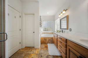 Full bathroom featuring a garden tub, double vanity, and stone tile flooring