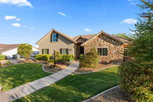 View of front of property with stone siding, a front lawn, stucco siding, and a tile roof