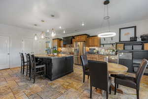 Kitchen featuring dark stone counters, a kitchen breakfast bar, a kitchen island with sink, decorative light fixtures, and appliances with stainless steel finishes