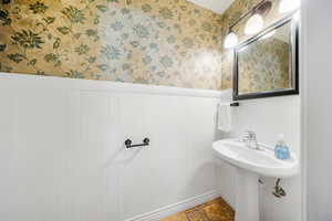 Bathroom with a wainscoted wall, wallpapered walls, and stone finish flooring