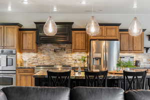 Kitchen featuring backsplash, stainless steel appliances, brown cabinets, dark stone countertops, and recessed lighting