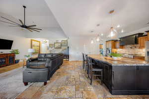 Kitchen with a ceiling fan, light stone countertops, a breakfast bar, a large island with sink, and custom exhaust hood