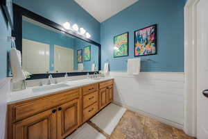 Full bath featuring double vanity, a wainscoted wall, and light stone finish flooring