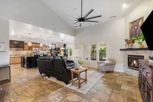 Living area featuring a ceiling fan, a stone fireplace, high vaulted ceiling, recessed lighting, and stone tile floors