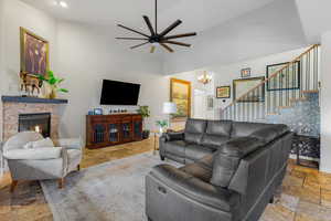 Living room with stone tile flooring, a chandelier, a fireplace, a ceiling fan, and a towering ceiling