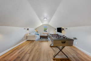 Recreation room featuring light wood-style floors, a textured ceiling, and lofted ceiling