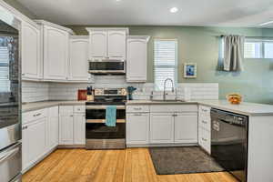 Kitchen with stainless steel appliances, light wood-type flooring, white cabinets, and recessed lighting