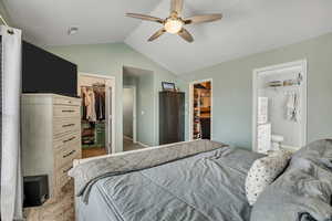 Bedroom featuring a walk in closet, vaulted ceiling, light colored carpet, ensuite bathroom, and ceiling fan