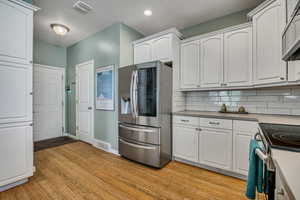 Kitchen with stainless steel appliances, light wood finished floors, and white cabinetry
