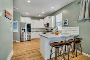 Kitchen with stainless steel appliances, a peninsula, light wood-type flooring, a breakfast bar area, and white cabinets