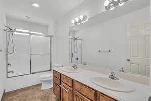 Full bath with bath / shower combo with glass door, double vanity, light tile patterned floors, and recessed lighting