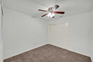 Unfurnished bedroom with dark carpet, a closet, and a ceiling fan