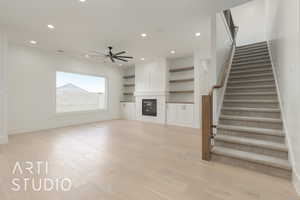Unfurnished living room with a ceiling fan, light wood finished floors, stairs, recessed lighting, and a glass covered fireplace