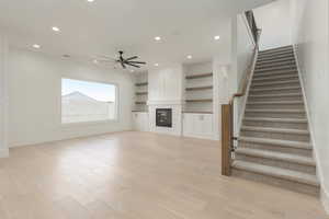 Unfurnished living room with light wood-style floors, recessed lighting, stairs, and a glass covered fireplace