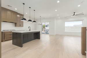Kitchen featuring hanging light fixtures, decorative backsplash, an island with sink, open floor plan, and light wood-style flooring