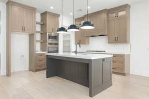 Kitchen with light wood-style flooring, a center island with sink, appliances with stainless steel finishes, light stone counters, and recessed lighting