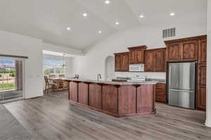 Kitchen featuring white appliances, light countertops, a breakfast bar, light wood finished floors, and high vaulted ceiling