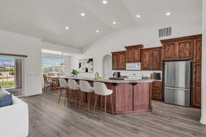 Kitchen with white appliances, a breakfast bar area, high vaulted ceiling, light countertops, and light wood-type flooring