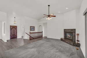 Unfurnished living room with arched walkways, ceiling fan, high vaulted ceiling, a high end fireplace, and carpet flooring